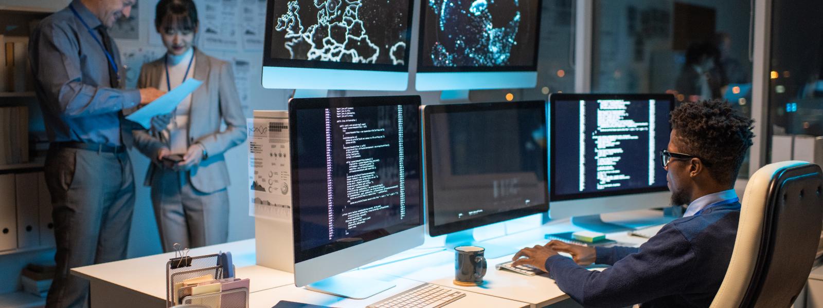 Mann sitzt an einem Computer mit mehreren Bildschirmen